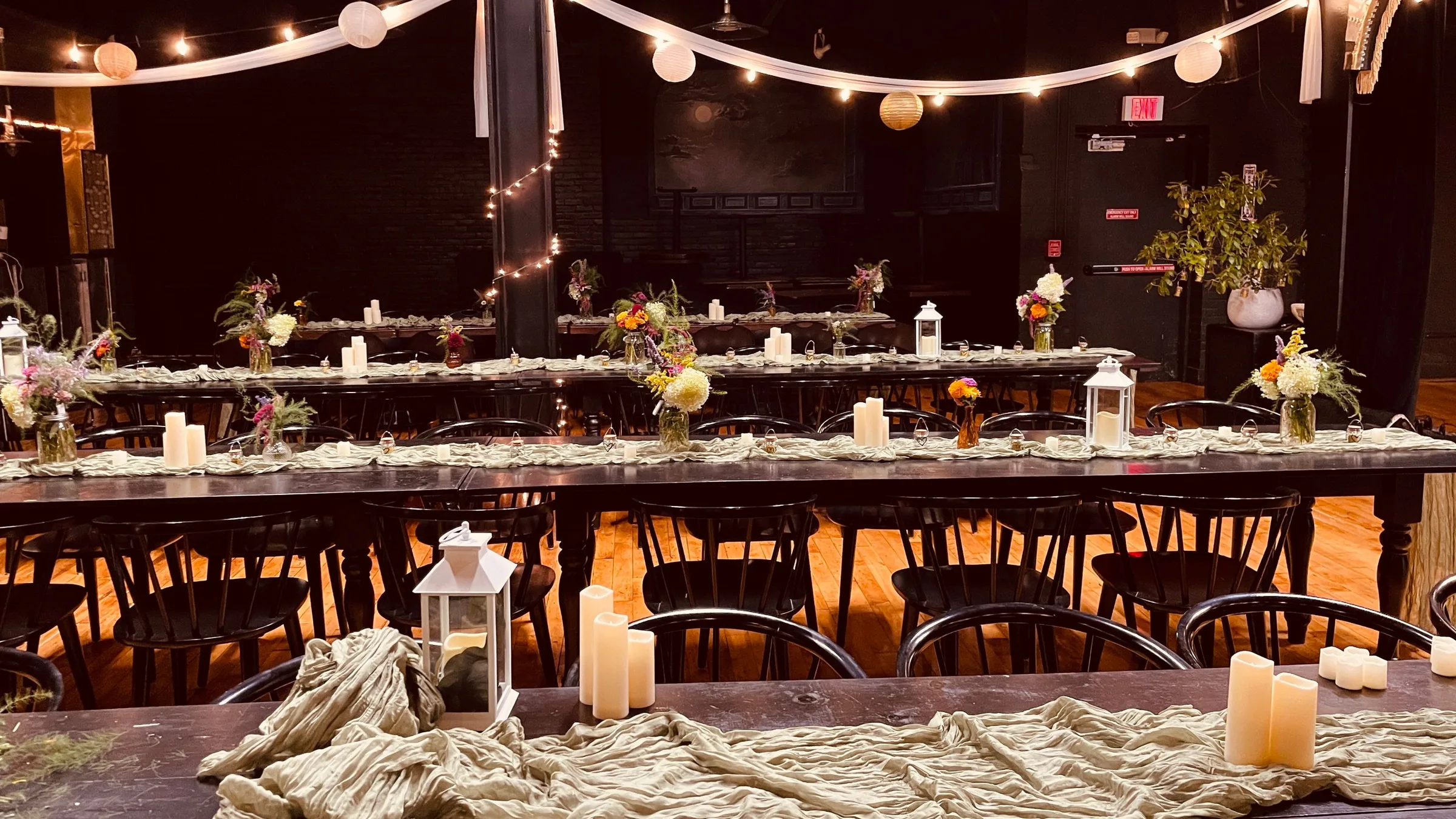 Long wooden tables set with candles, lanterns, wildflowers and linen runners under swags of fabric and string lights