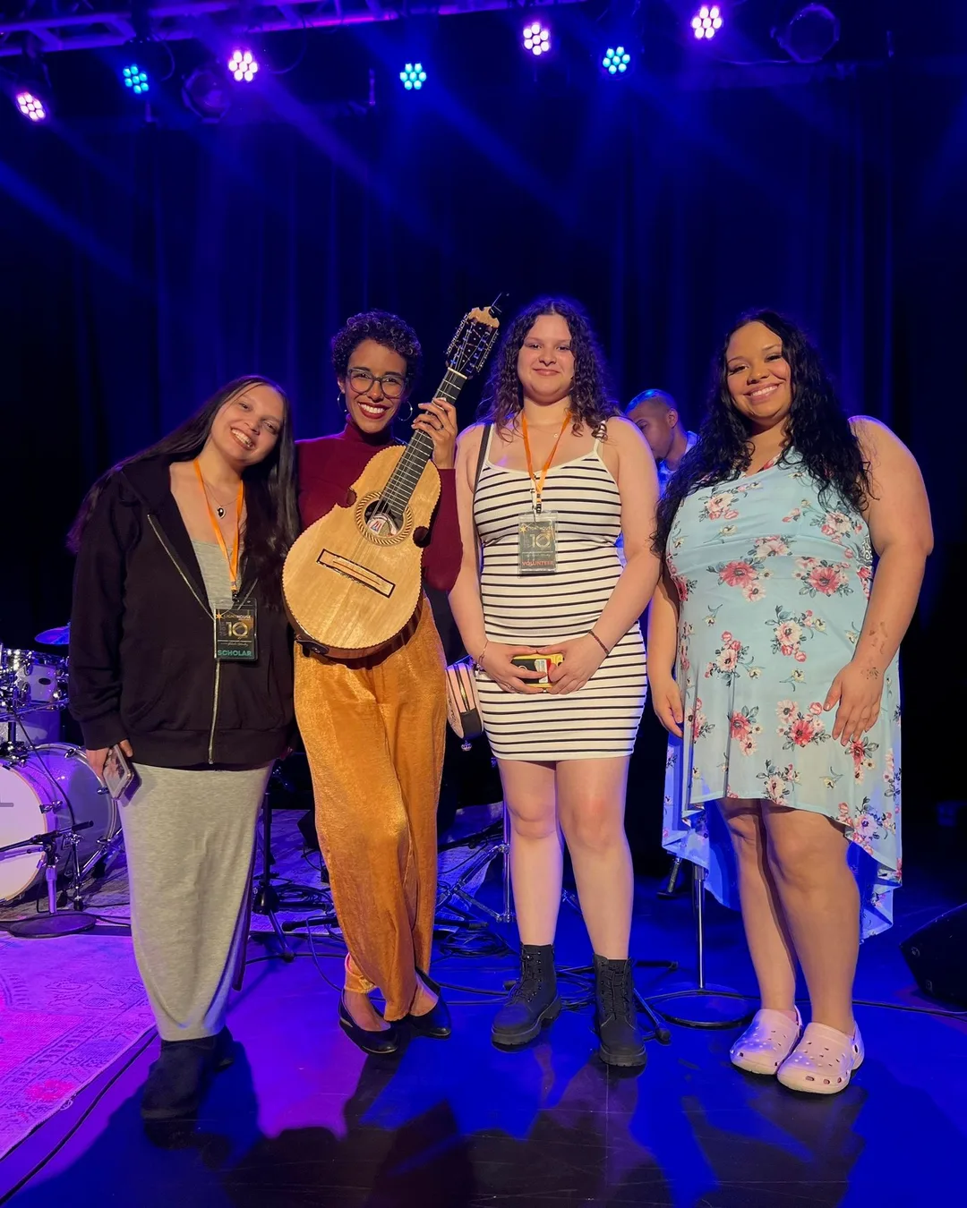 Fabiola Méndez holding a cuatro on stage with three young women from the Technical Arts program