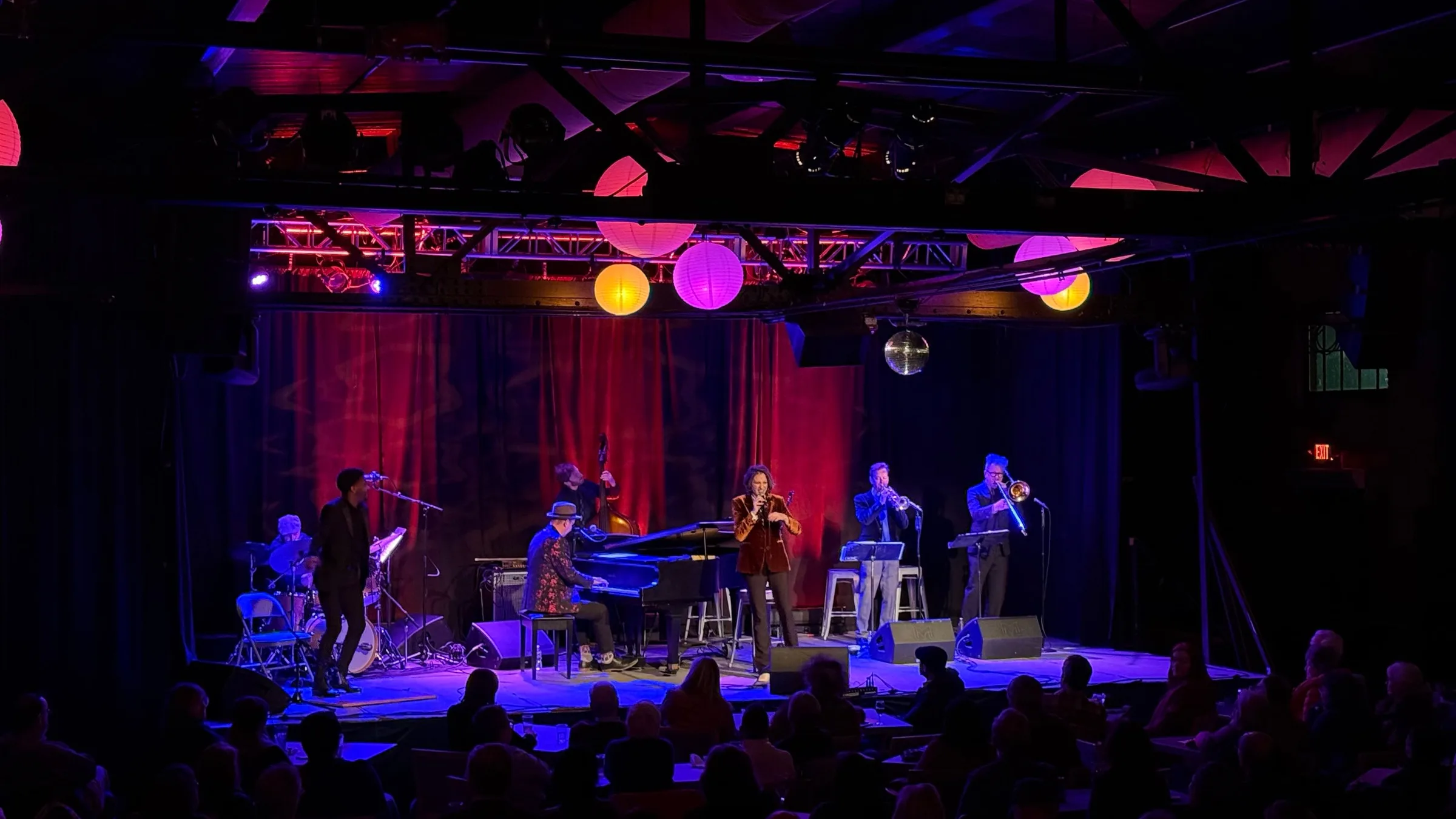 A band with a grand piano and horns on the Soundstage, seen over a full room of guests at tables