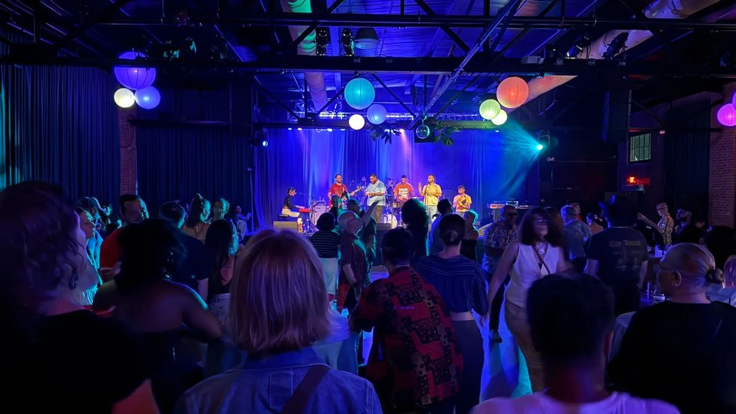 A crowd on the Soundstage floor facing a band under blue light and coloured paper lanterns