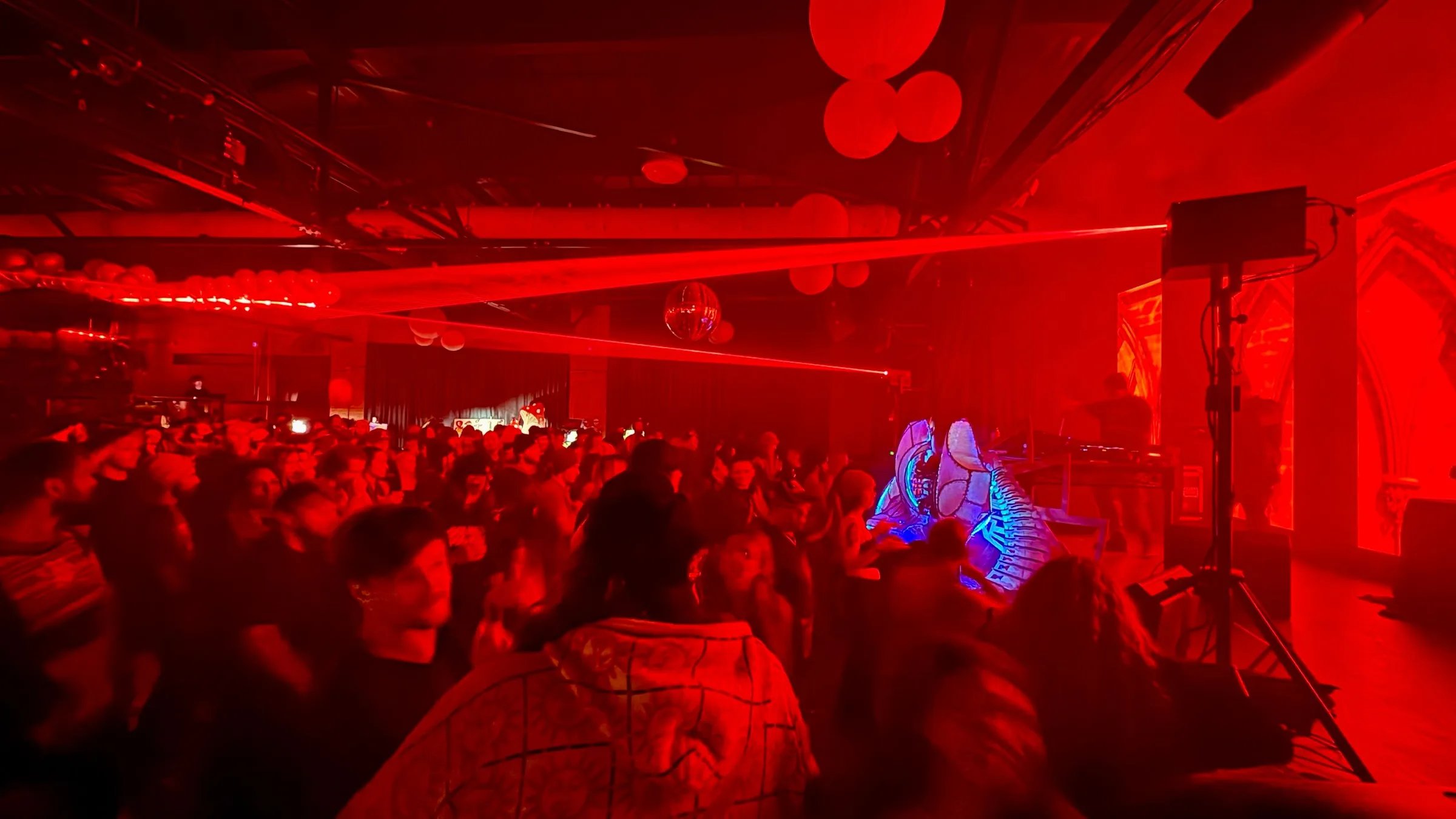 A dance floor bathed in red light, a laser across the room and paper lanterns overhead