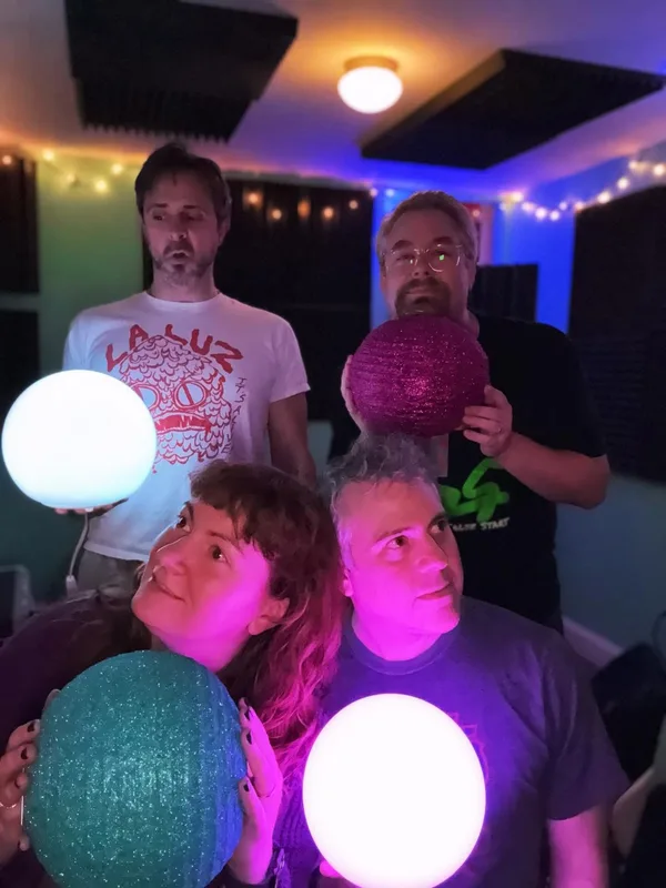 Four people holding glowing spheres in an indoor venue lit with purple and blue stage lighting.