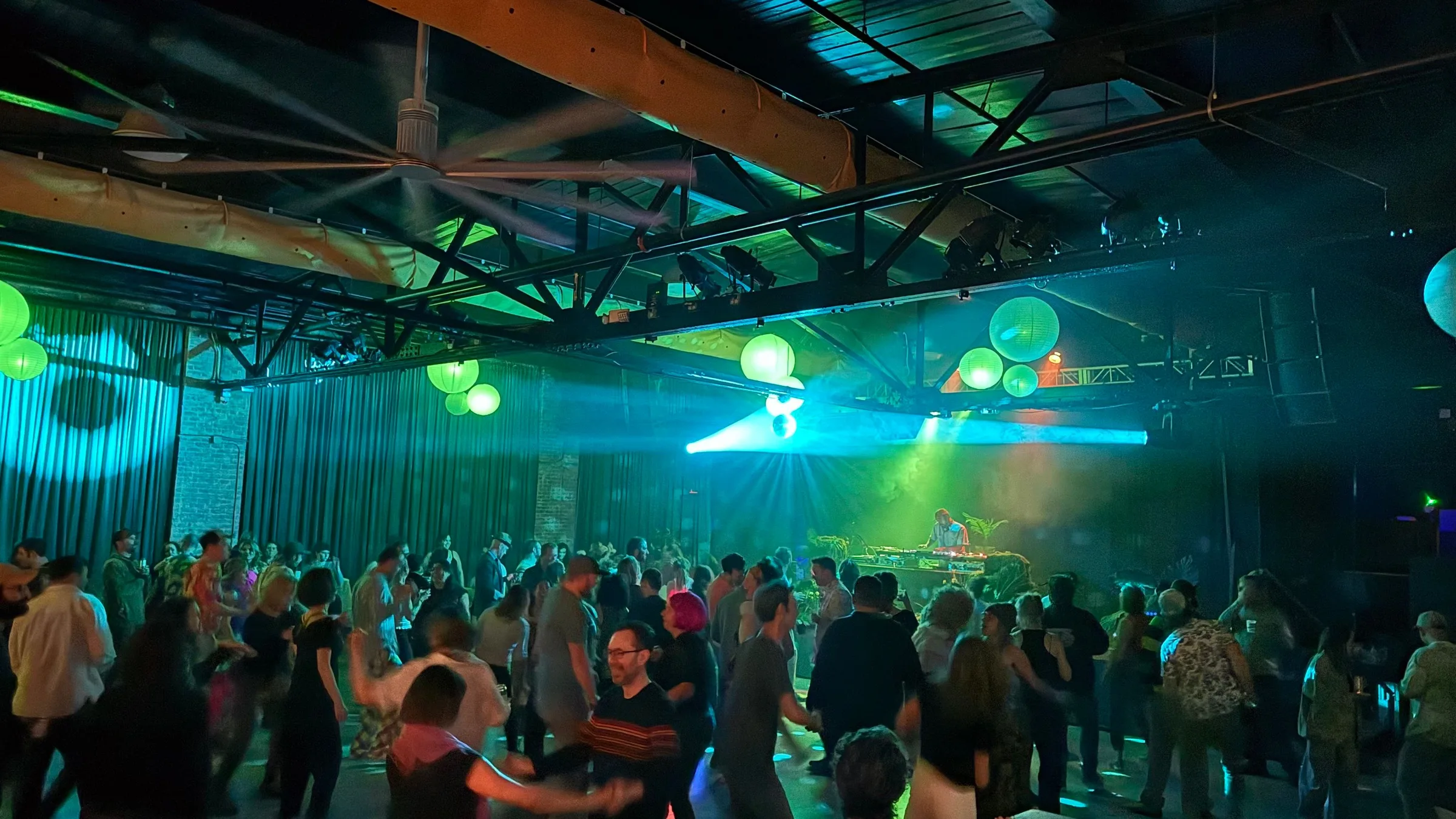 Couples dancing on an open floor in green and blue light, a DJ at the far end of the room